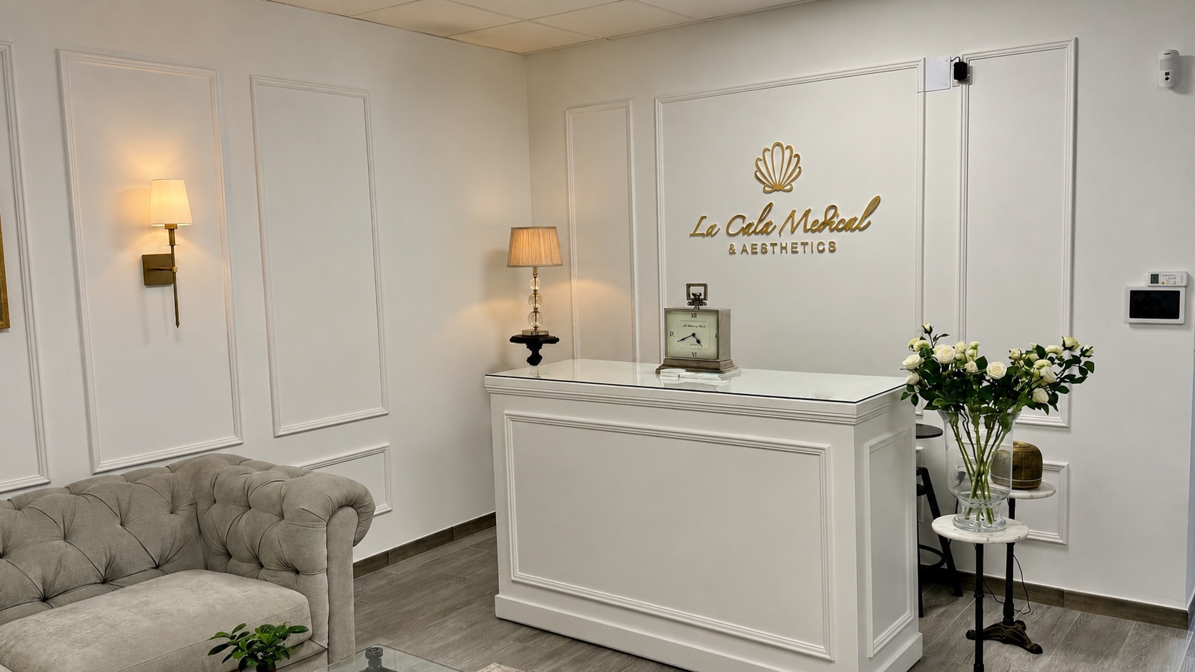 The reception and waiting room at La Cala Medical & Aesthetics, with the clinic's gold shell logo on a white panelled wall.